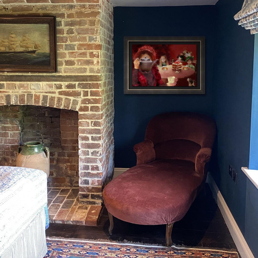 A framed art print depicting a whimsical tea-time scene with a sinister and dark tale, hung on a dark blue wall above a dusty rose velvet chaise lounge in a rustic room with a brick fireplace.