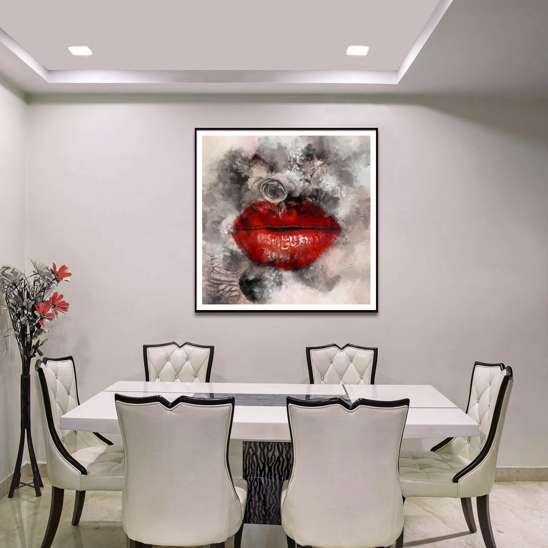 A framed abstract wall art print featuring a bold red lips motif with gray, black, and white smoky brushstrokes, displayed above a white dining table with white upholstered chairs in a modern dining room.